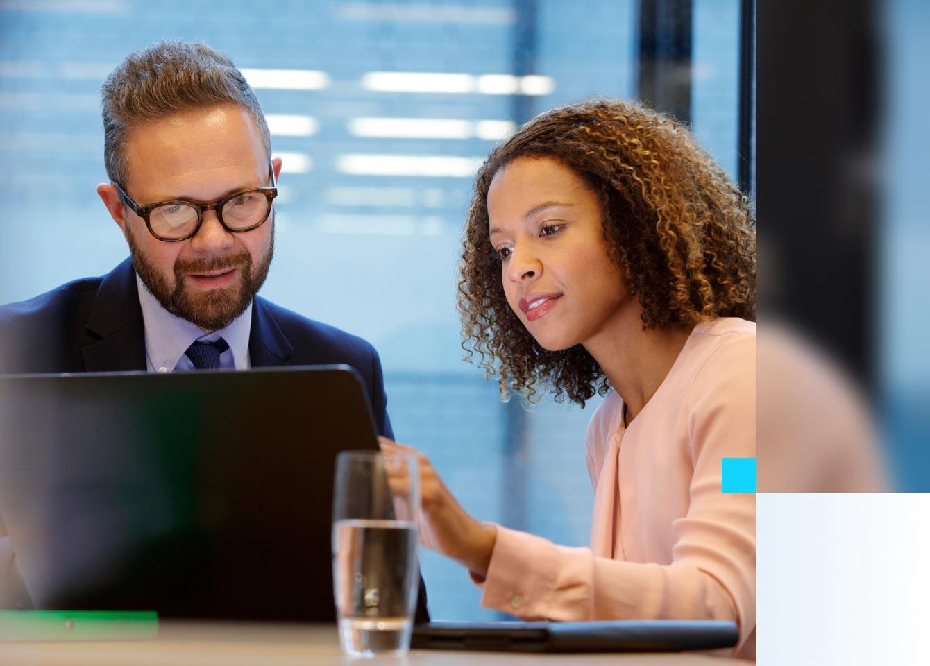 A businesswoman and businessman analyze data on a laptop, focusing on risk management and vulnerability insights.