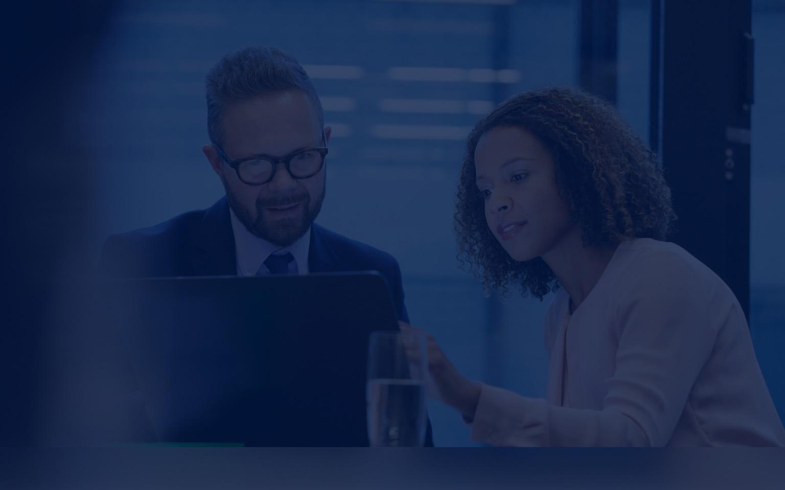 A businesswoman and businessman analyze data on a laptop, focusing on risk management and vulnerability insights.