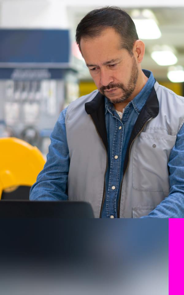A man focused on his laptop in a warehouse, symbolizing the intersection of technology and industry in cybersecurity.