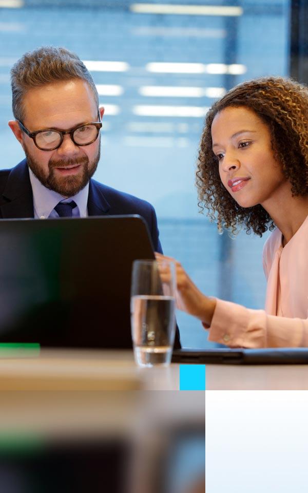 A businesswoman and businessman analyze data on a laptop, focusing on risk management and vulnerability insights.