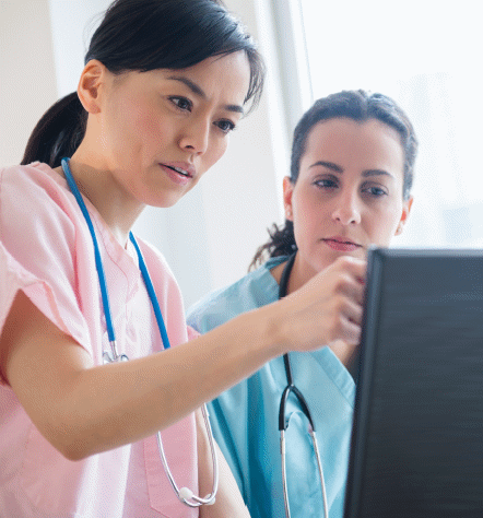 A doctor and nurse look at a shared workstation in a hospital room.