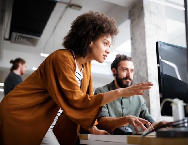 A woman and man collaborate on a computer in an office, enhancing threat detection and response through integrated technology.