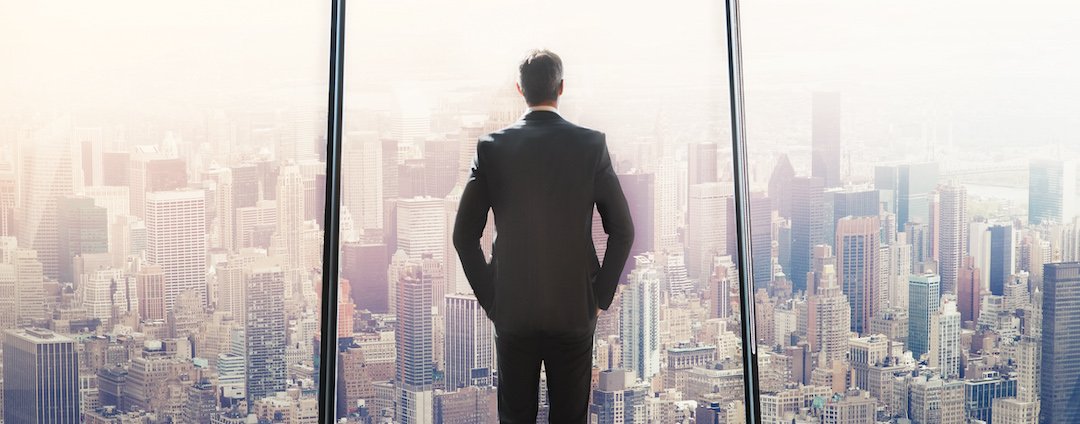 A man in a suit looks out of a high rise building