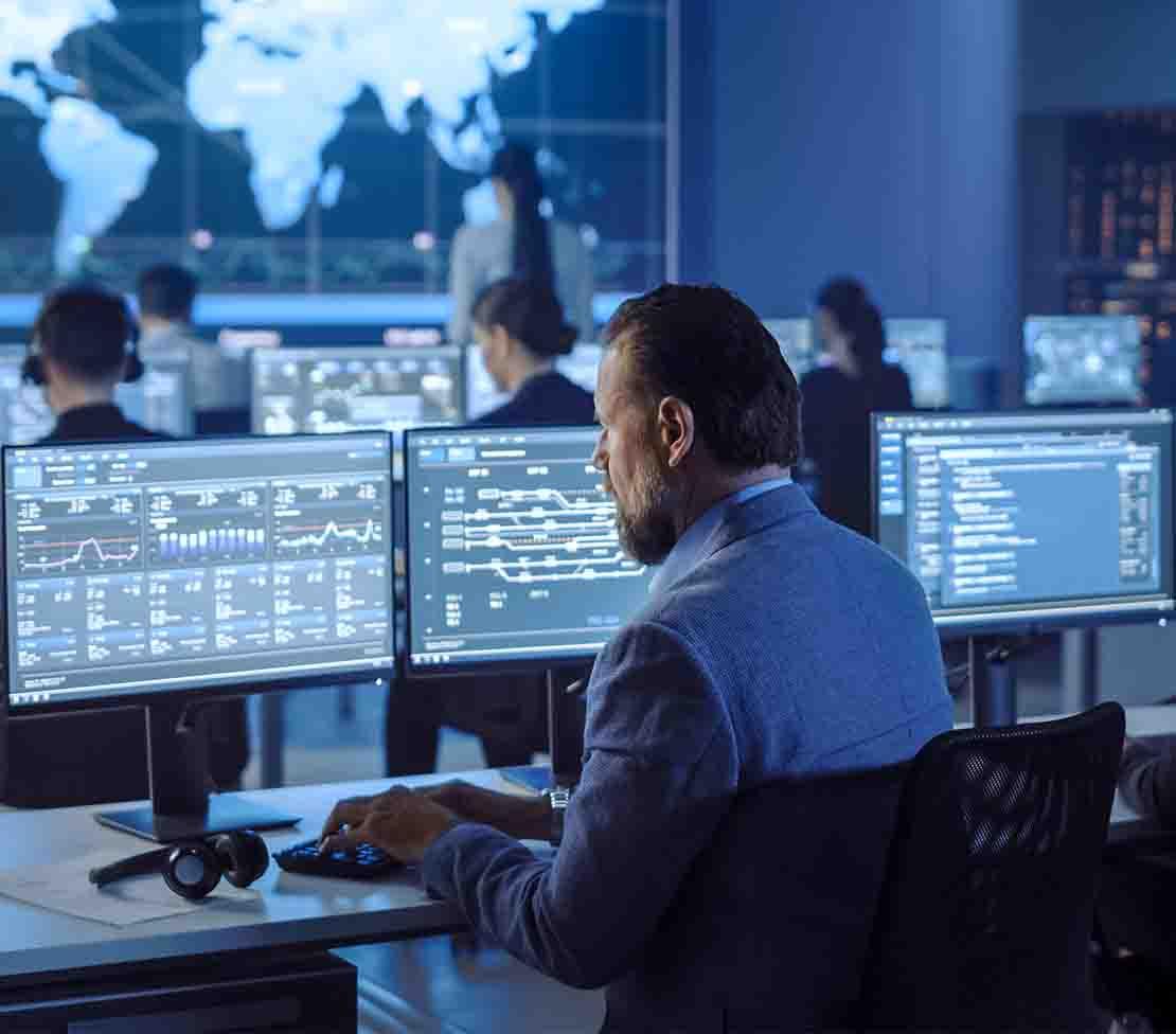 A suited man at a desk with several monitors, engaged in risk management and vulnerability assessment tasks. A suited man at a desk with several monitors, engaged in risk management and vulnerability assessment tasks.