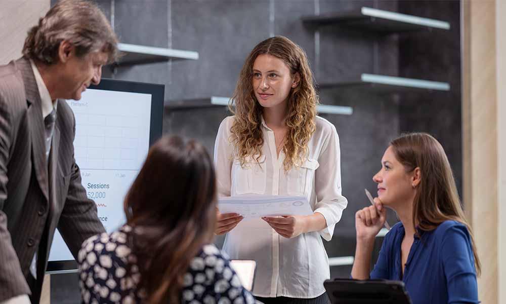 Breadth of integrations A woman addresses a group in an office setting, discussing strategies for integrating vulnerability data and risk management.