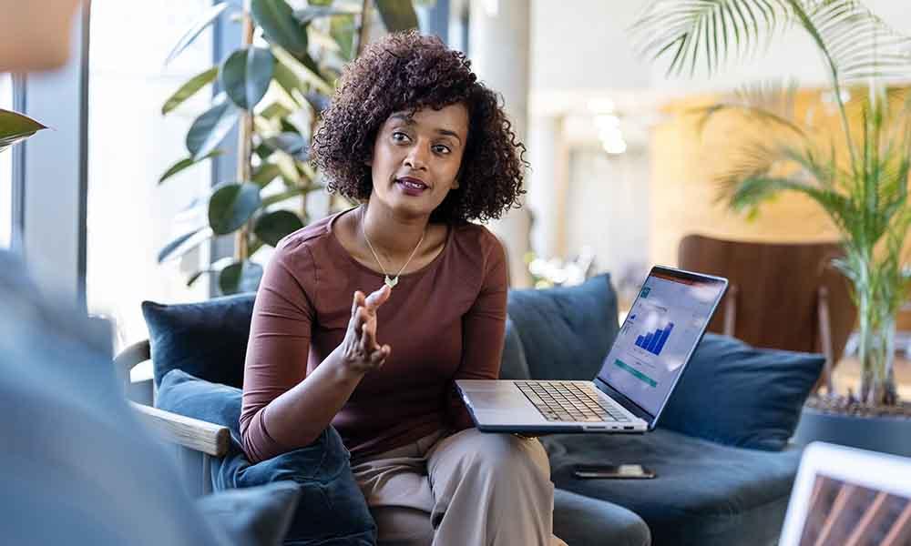 Customizable reporting In an office, one woman speaks to another, highlighting dynamic dashboards and reports for security and performance metrics.